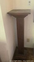 Full view of the wooden plant stand against a wall showing its height and square top