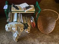 Full lot view showing garden work seat with assorted books underneath, two small garden figurines, decorative garden wall planter, and large woven basket.