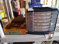 Wide view showing black plastic storage organizer with labeled drawers and yellow metal box containing electric drill.