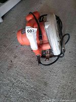 Side view of handheld Black & Decker circular saw with orange casing, metal blade guard, and attached power cord.