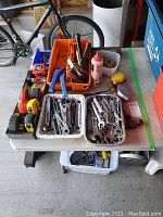 Wide view of table showing multiple trays of wrenches, measuring tapes, plastic bins with tools, chalk line dispenser and related hardware