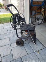 Side view of black and silver pressure washer with coiled hose and spray wand, wheels and handle visible