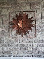 Front view of metal flower wall art with layered petals inside a square frame on a stone wall.