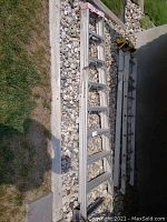 Full length view of aluminum ladder lying on pebbled ground and grass. Shows entire ladder and structure with aluminum rungs.