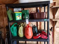 Wide view of the black plastic shelving with gardening tools and accessories including watering cans, fertilizer containers, hand-held spreader, and other items