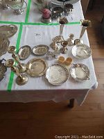 Overview photo of table with silver plated candlesticks, napkin rings, and various serving dishes arranged for sale.