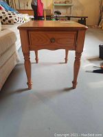 Front view of the wooden end table showing drawer and turned legs