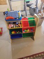 Overview photo of the wooden organizer with seven colored plastic bins in blue, green, yellow, and red, filled with assorted children's toys.