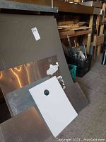 Photo shows a pile of scrap metal sheets leaning against a wall with wood scrap behind them. The sheets vary in size and finish with some rust and peeling paint.