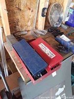 Photo shows two metal socket set cases, one blue and one red, placed on a wooden surface along with some wood clamps around.