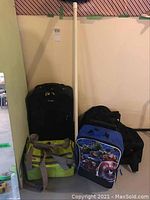 Four travel bags: black rolling suitcase, green and gray cooler bag, blue and black superhero rolling bag, and large black duffle bag.
