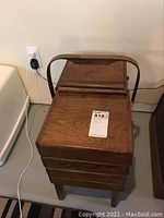 Front view of the closed wooden fold-out sewing basket with handle and legs.