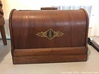 Closed wooden carrying case, front view with gold Singer trademark decal.