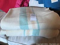 Two cream colored Kenwood wool blankets folded, showing blue and tan vertical stripes.