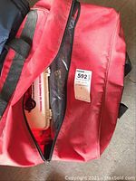 Red emergency carry bag slightly open showing multiple emergency supplies inside including a plastic first aid kit case.