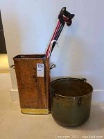 Photo showing rectangular brass/copper bin with walking sticks and round brass bin side by side