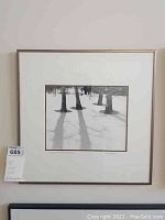 Framed black and white photograph showing snow, tree trunks and shadows; simple white mat and frame