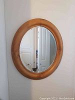 Full view of an oval mirror with a smooth wooden frame hung on a wall reflecting interior room details.