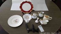 Full view of assorted china on table including plates, small pitcher, vase, sugar bowl, and ruffled dish.