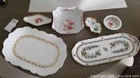 Wide view of six assorted porcelain dishes including floral patterns and gold leaf decoration showing various shapes and sizes.