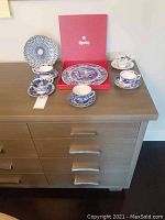 Five teacups with saucers and plates arranged on a cabinet, showing the full lot contents including Spode plate in box and blue patterned plates.