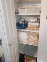 Photo of a shelf containing folded stacks of linens and towels along with a small vintage iron in a plastic blue container