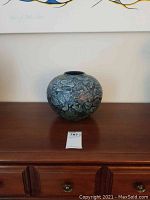 Round stoneware vase with abstract textured blue, green, and black pattern, displayed on wooden dresser.