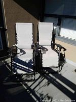 Two matching white zero gravity lounge chairs positioned side by side, showing full front views and sturdy black metal frames.