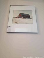Framed watercolor painting showing red barns in winter snow landscape from a distance on a wall.