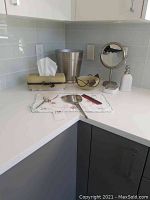Photo of entire lot including silver plated vanity pieces, standing mirror, soap dispenser, metal wastebasket, sunglasses, comb, and embroidered cloth.