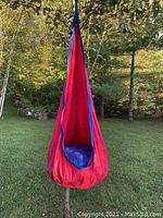 Front view of a child size hanging cocoon chair made from red and blue fabric, hanging outdoors from a tree branch.