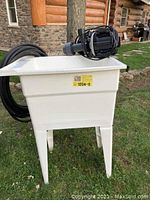 Laundry tub standing outdoors on grass with pump placed on top