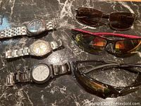 Photo showing three men's watches and three pairs of men's sunglasses arranged on marble surface