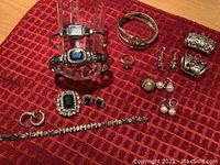 Various vintage costume jewelry items including bracelets, rings, earrings, and a wristwatch arranged on a red textured cloth.