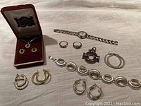 Full lot view showing various pairs of earrings, rings, bracelets, a watch, and pendants on a light fabric background.