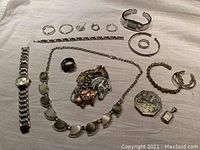 Photo of entire lot on white fabric including watches, bracelets, necklaces, brooches, rings, earrings, and pendants