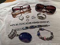 Photo shows all items in the lot including sunglasses, reading glasses, wristwatch, bracelets, rings.