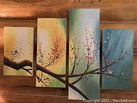 Photo showing set of four oil on canvas vertical paintings of flowering tree branches, arranged side by side on wooden surface.