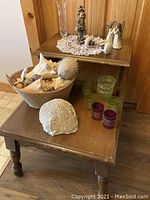 End table with large seashells in a basket on lower shelf, assorted glass candle holders, and figurines on the top shelf.