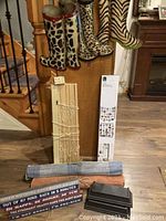 Photo showing rubber boots hanging on a stair rail, wooden window blinds leaning against wall, two rolled mats, and a wire photo hanger set on the floor.