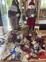Wide view of multiple Christmas decorations including two large dolls, decorative star, wreaths, and assorted ornaments spread out on a tabletop.