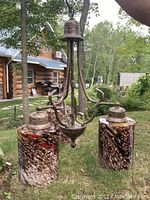 Hanging light fixture with three arms and three cylindrical brown, cream, and red patterned glass shades suspended outdoors.