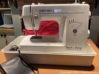 Full front view of the Euro-Pro X Fast & Easy sewing machine in white with foot pedal in plastic tray base.