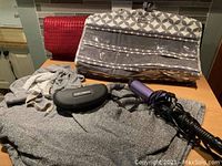 Photo showing grey H&M hoodie, Dolce & Gabbana sunglasses in black case, purple curling iron, jewelry hanging bag on a wooden surface.