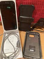 Samsung Galaxy A5 phone on box showing quick start guide with charging cable coiled, OtterBox phone case with belt clip, and charging adapter partially visible.