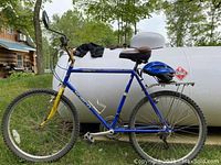 Full view of blue Norco mountain bike outdoors with helmet and bike shorts lying on tank in background.