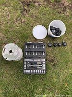 Photo showing the socket set case open with sockets and ratchet, the spool of electrical wire, and a white bucket with wheels on grass.