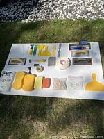 Top-down photo of assorted tile tools, sponges, drywall tape, and plastic tile spacers arranged neatly on a white surface outdoors