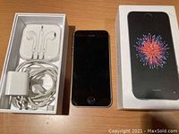 Silver iPhone SE smartphone with accessories and original box on wood surface.