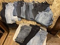 Image of folded ladies jeans and a jean shirt on a couch, showing various sizes and washes.